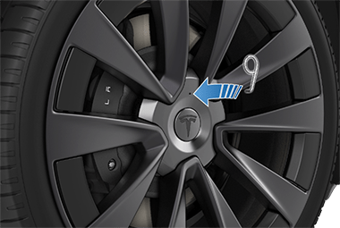 Šipka směřující od nástroje na matice kol k otvoru na krytu matice kol